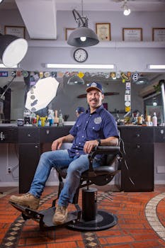 Man sitting in a stylish barbershop armchair, smiling at camera.