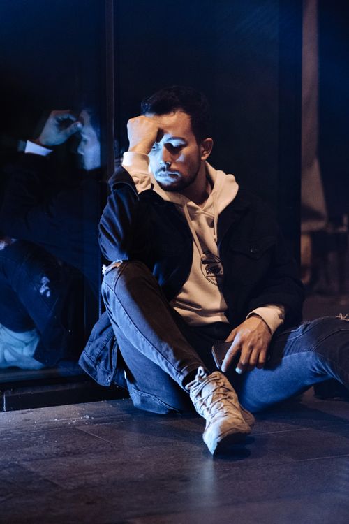 Free A young man sits on the floor, reflecting with a hand on his forehead, conveying deep thought and emotion. Stock Photo