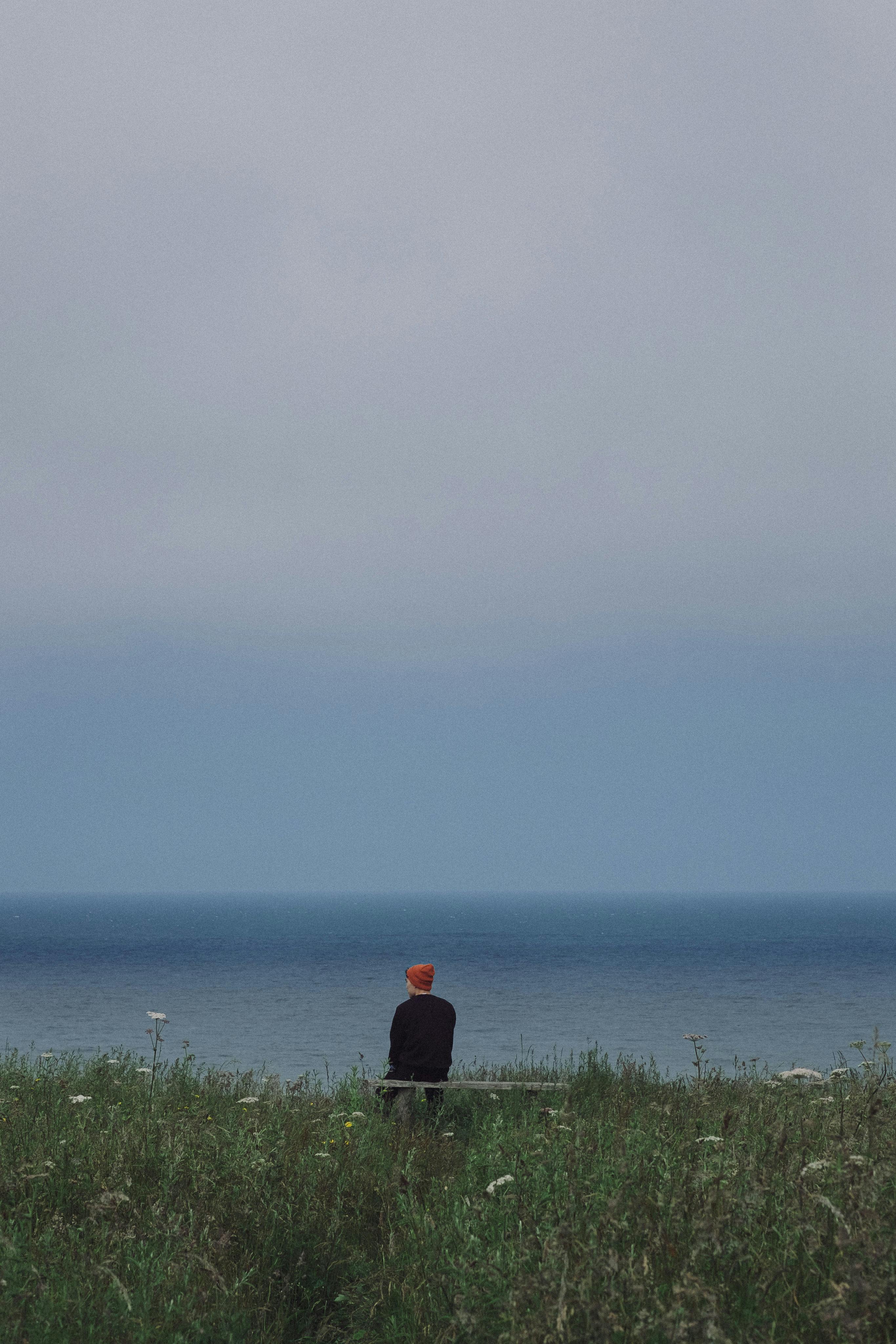 孤独的人坐在长椅上，凝视着宁静的海洋地平线