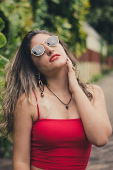 一位身穿红色上衣、戴着太阳镜的年轻女子在户外自信地摆着姿势，展现出独特的风格