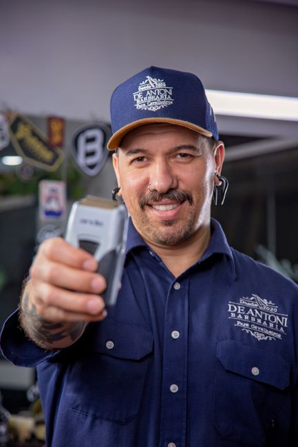 Smiling barber with mustache holds clippers in a modern barbershop.