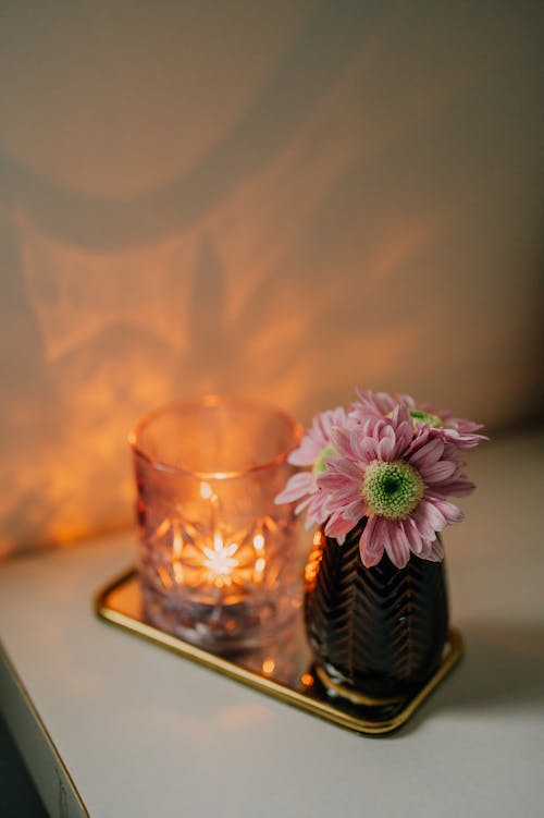 Pink Flowers in a Vase on a Golden Tray Next to a Candle in a Rocks Glass