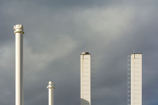 Three industrial chimneys stand tall against a dramatic cloudy sky, symbolizing industry and air pollution.