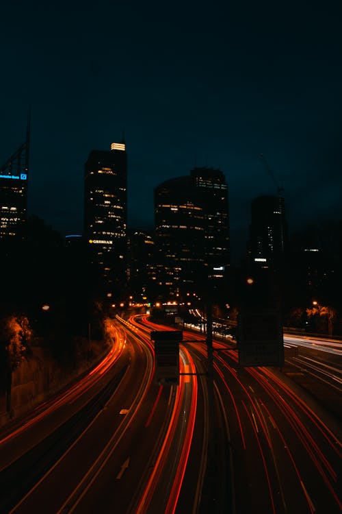 Kostenlos Zeitrafferfoto Der Beleuchteten Autobahn Bei Nacht Mit Gebäuden Im Hintergrund Stock-Foto