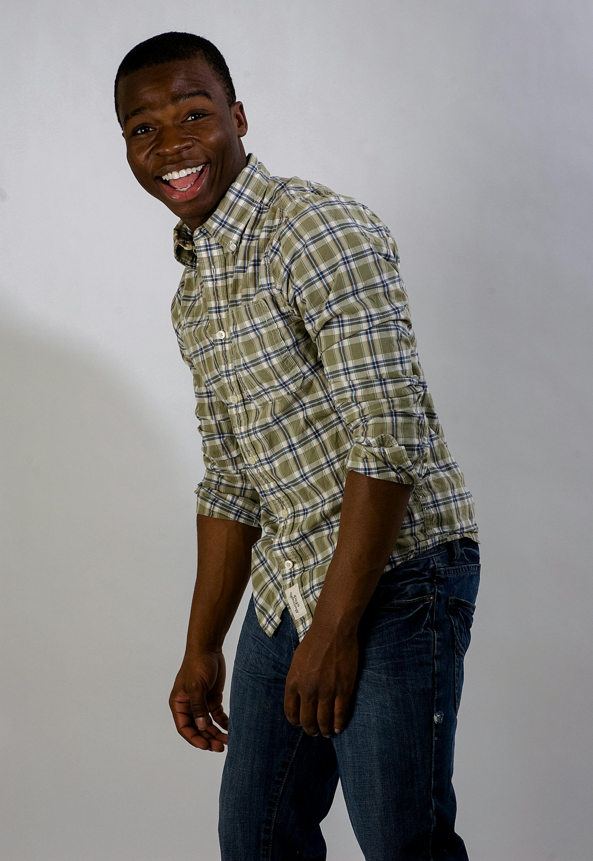 A joyful man wearing a checkered shirt posing and smiling in a studio setting.
