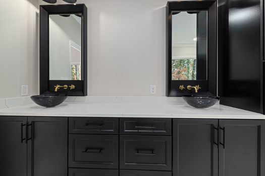 Elegant bathroom featuring black cabinets, vessel sinks, and gold hardware.
