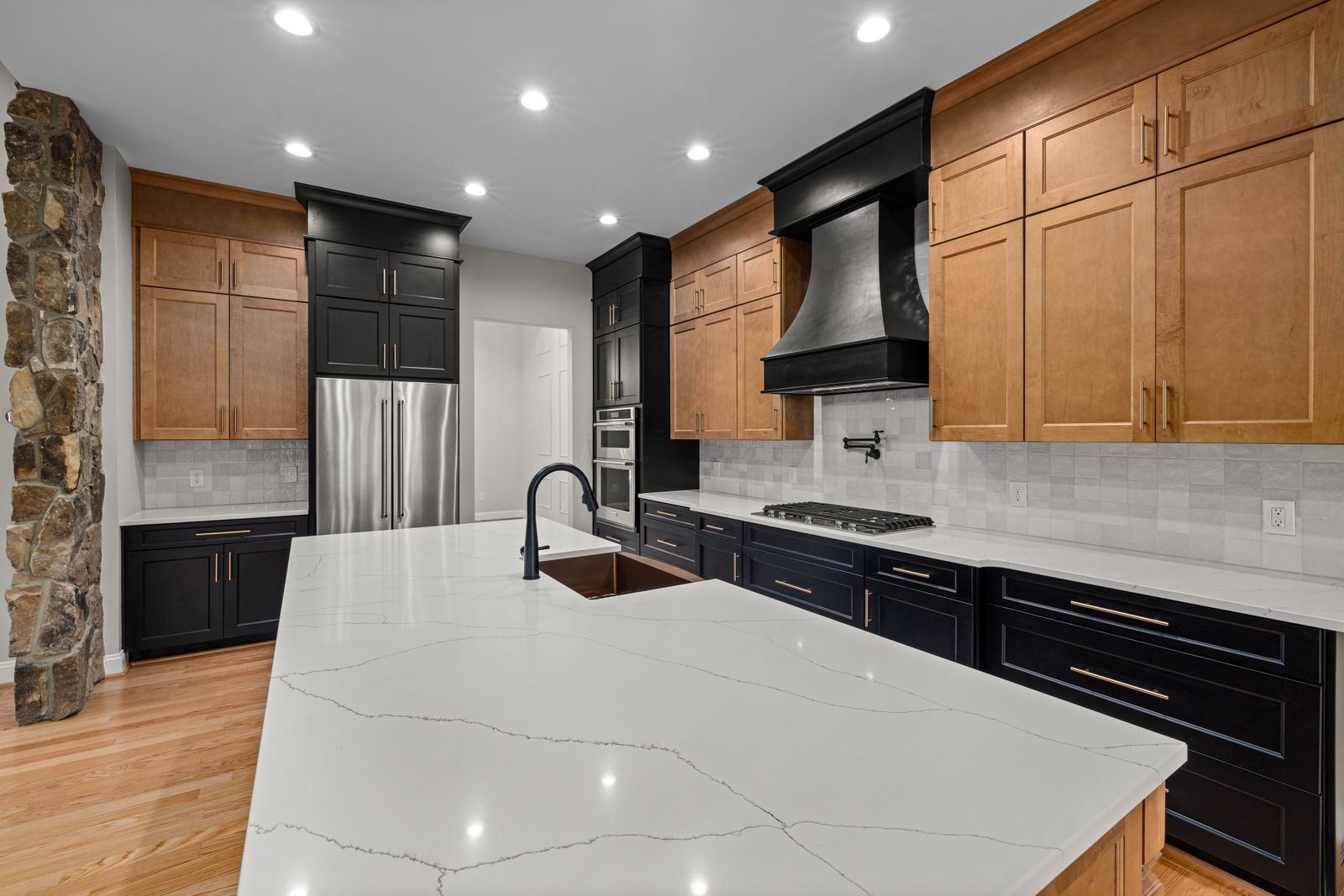Dark lower kitchen cabinets paired with natural wood uppers and pale stone-look counters.