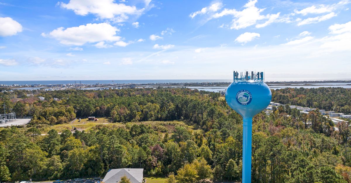 Aerial shot of Surf City's iconic blue water tower surrounded by lush greenery and coastal landscape.