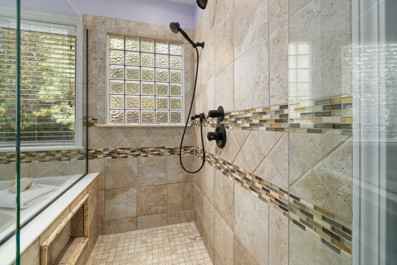 Travertine walk-in shower with a glass block window and mosaic tile border