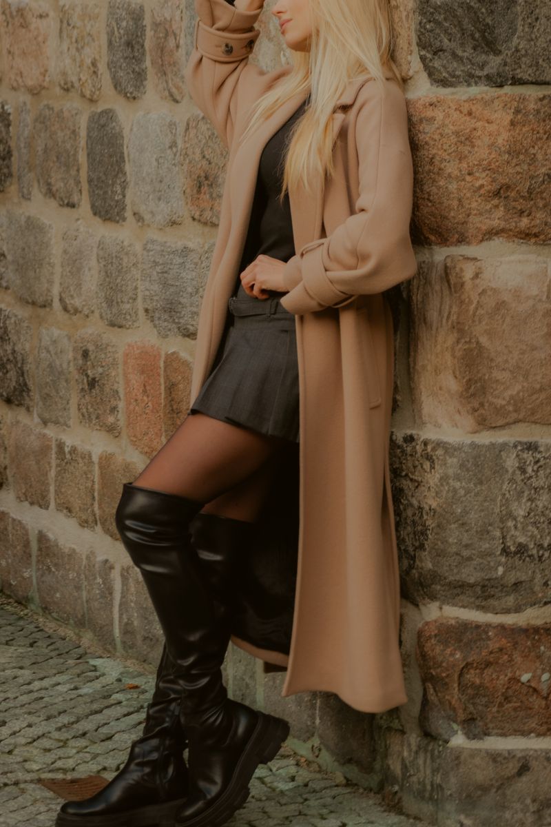 Woman in long coat and boots by stone wall