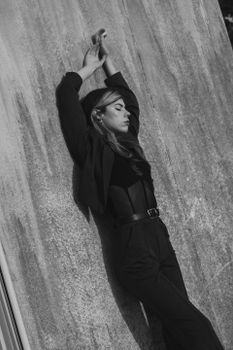 Fashionable woman posing against textured wall in black and white image.