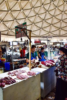 A vibrant scene at Chorsu Bazaar in Tashkent shows vendors selling fresh meat at a bustling indoor market.