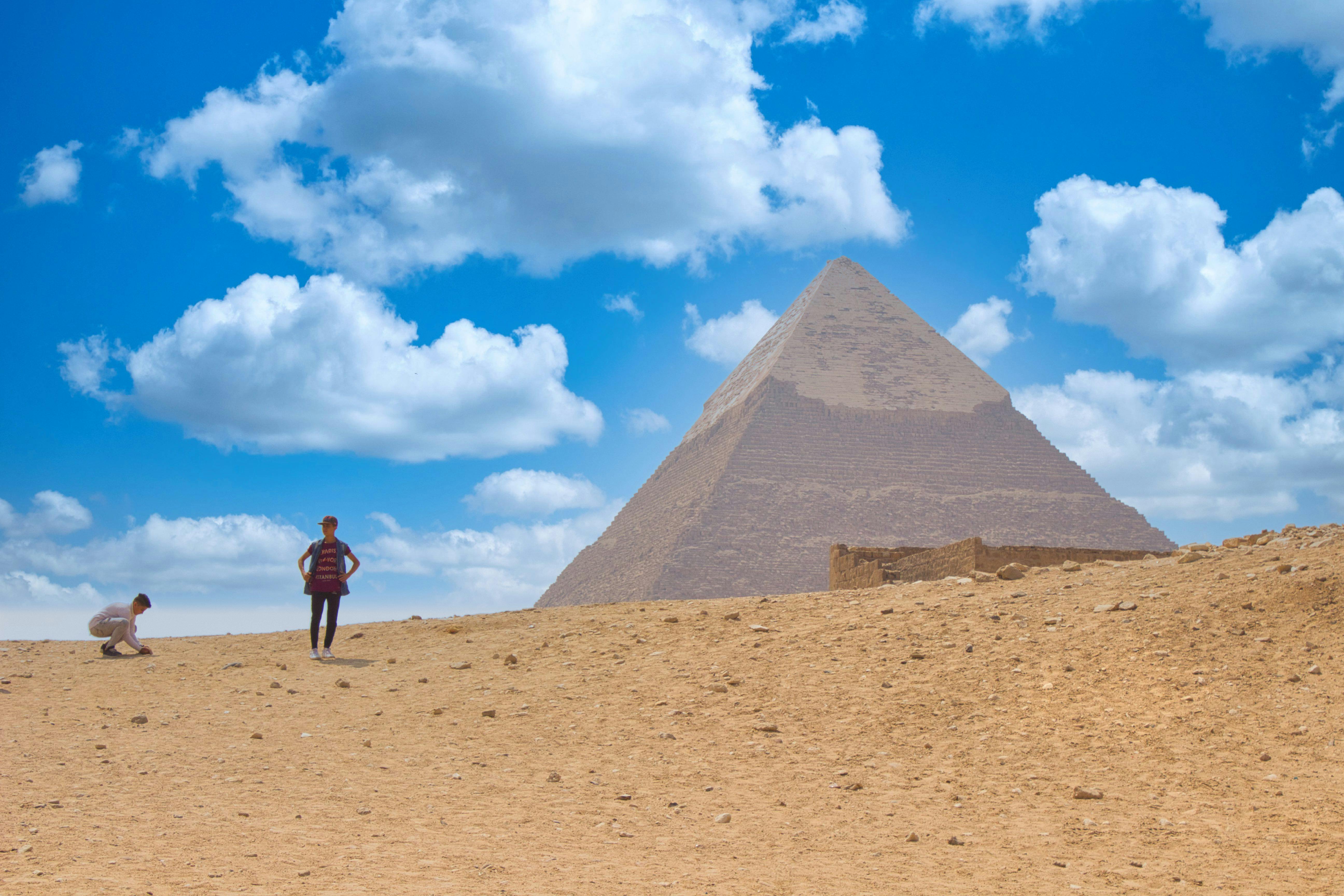 Tourists explore the desert landscape near the iconic Egyptian pyramid under a blue sky.
