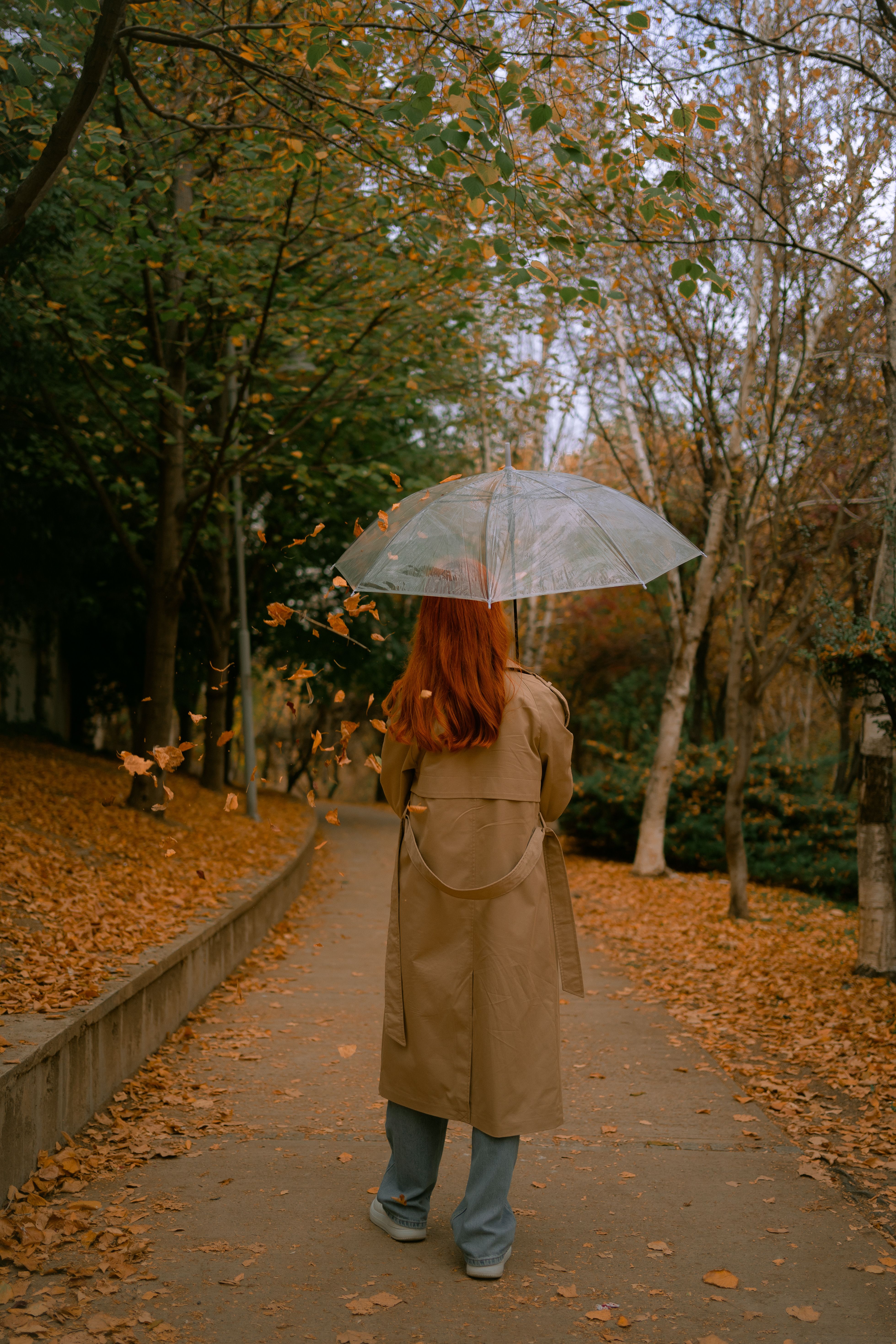 Woman in trench coat with umbrella in autumn park — how to layer outfits after 60