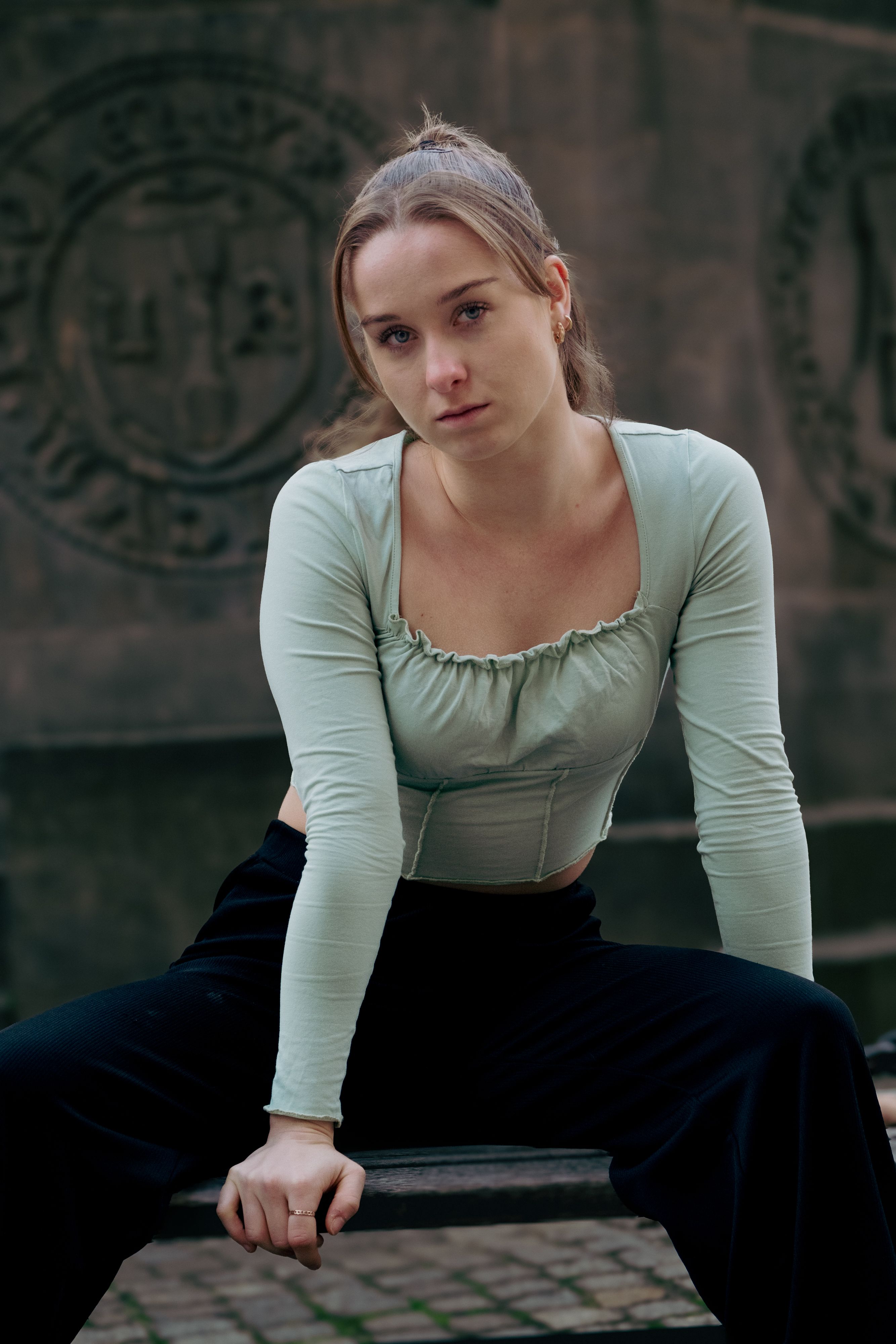 Stylish portrait of a young woman sitting outdoors, showcasing urban fashion with a relaxed pose.