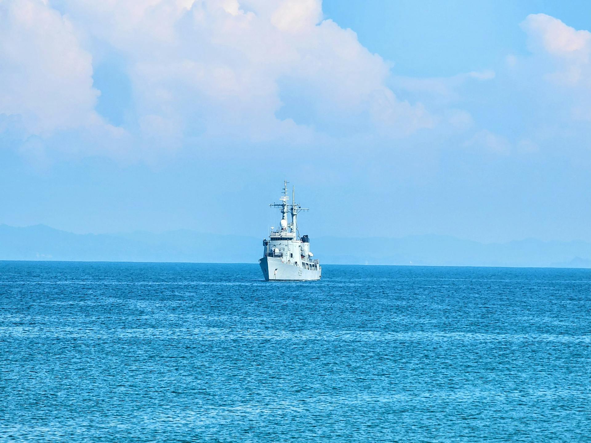 A naval vessel sailing across a calm blue ocean under a clear sky.