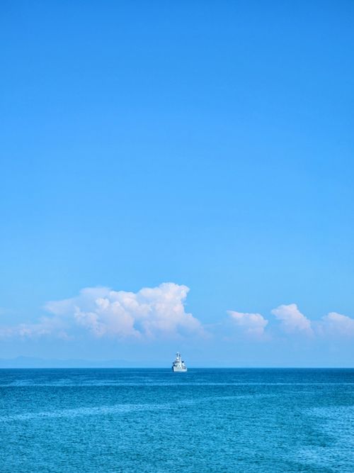 Free A ship sails on a calm ocean under a clear blue sky with fluffy clouds. Stock Photo