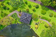 Experience the tranquility of lush gardens and a pond in Sukaresmi, Jawa Barat from above.