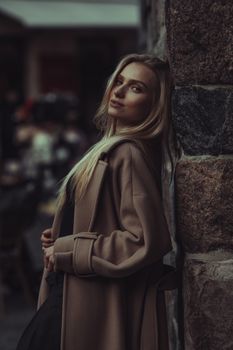 Stylishly dressed woman in Berlin, showcasing fall fashion while leaning on a stone wall.