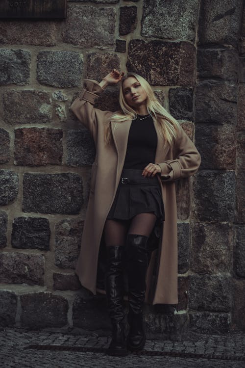 Young Fashionable Woman in a Coat Standing against a Stone Wall