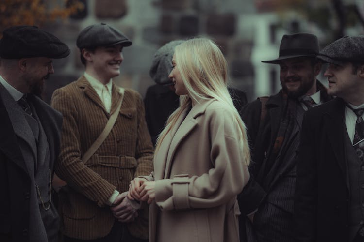 Woman Talking To A Group Of Men In Coats And Hats 