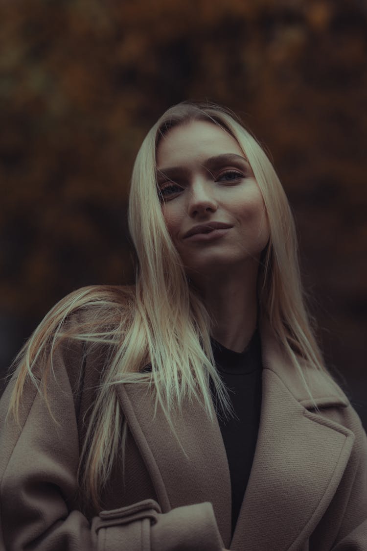 Young Woman In A Coat Standing Outside On The Background Of Autumnal Trees