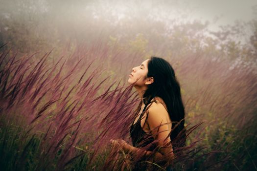 A serene young woman with eyes closed, basking in a mist-covered meadow, immersed in nature.