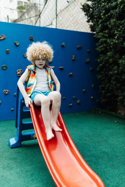 Free A cheerful child with curly hair plays on a slide in a colorful playground. Stock Photo
