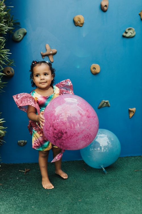 Free Adorable girl holding vibrant balloons against a climbing wall, enjoying outdoor fun. Stock Photo