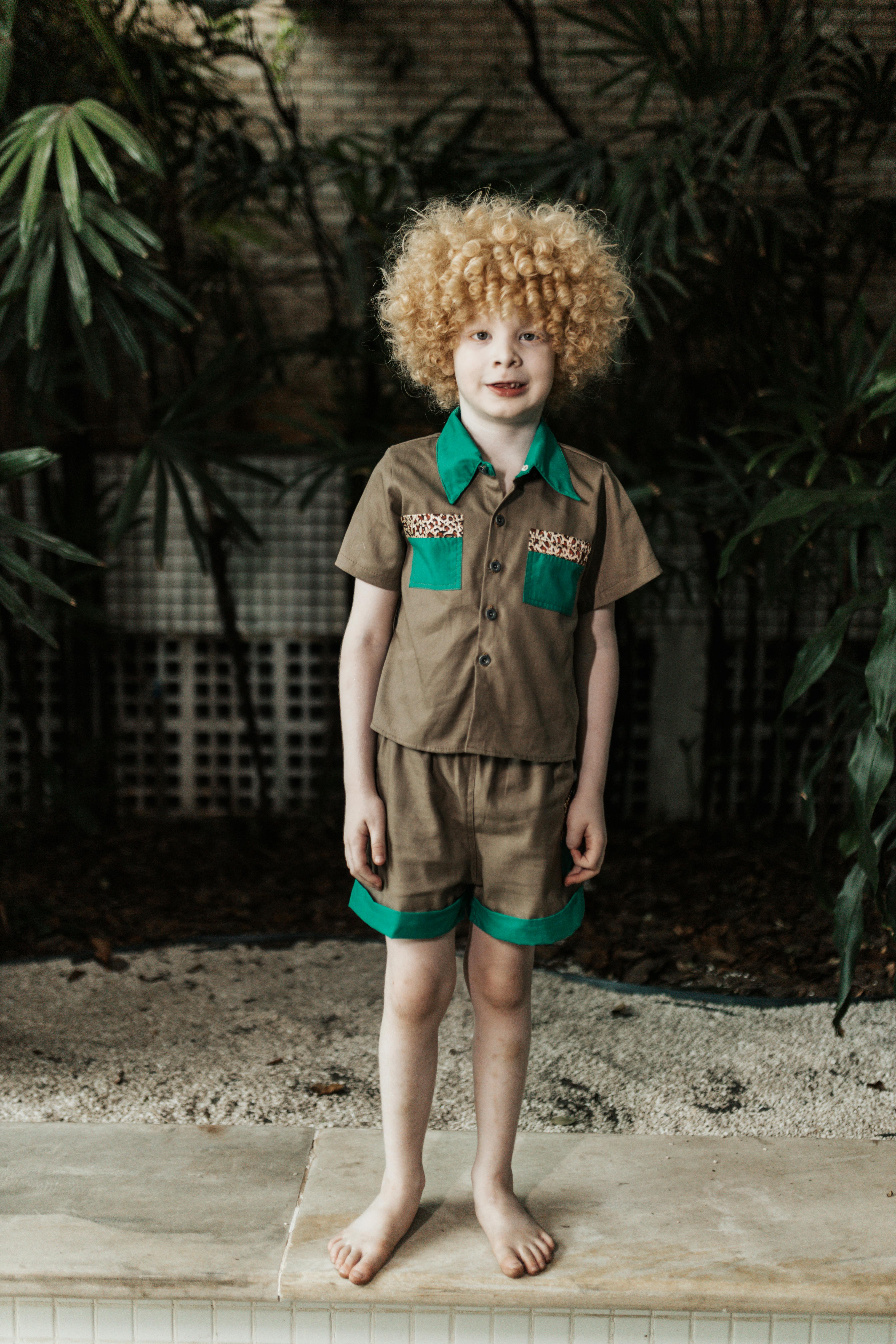 a little boy with curly hair standing near the plants