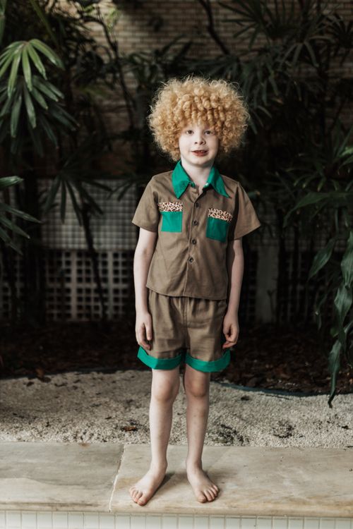 Free Cute child with curly hair in safari costume standing amidst tropical plants. Stock Photo