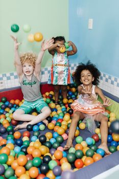 Three children having fun in a vibrant ball pit, exuding joy and energy.