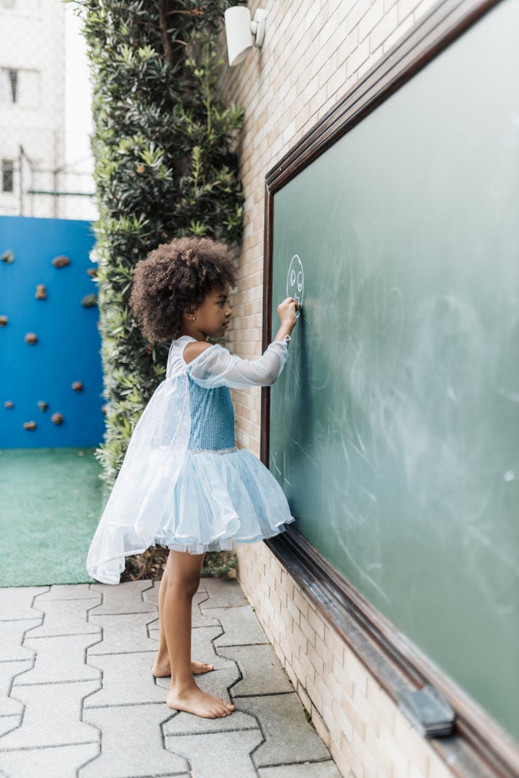 Child Model In Blue Dress Drawing With Chalk