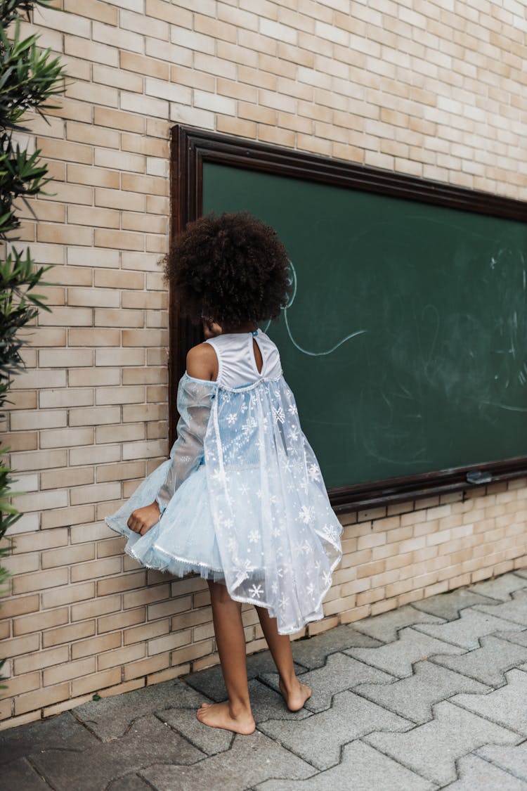 Young Girl In Lacy Dress Drawing On A Blackboard