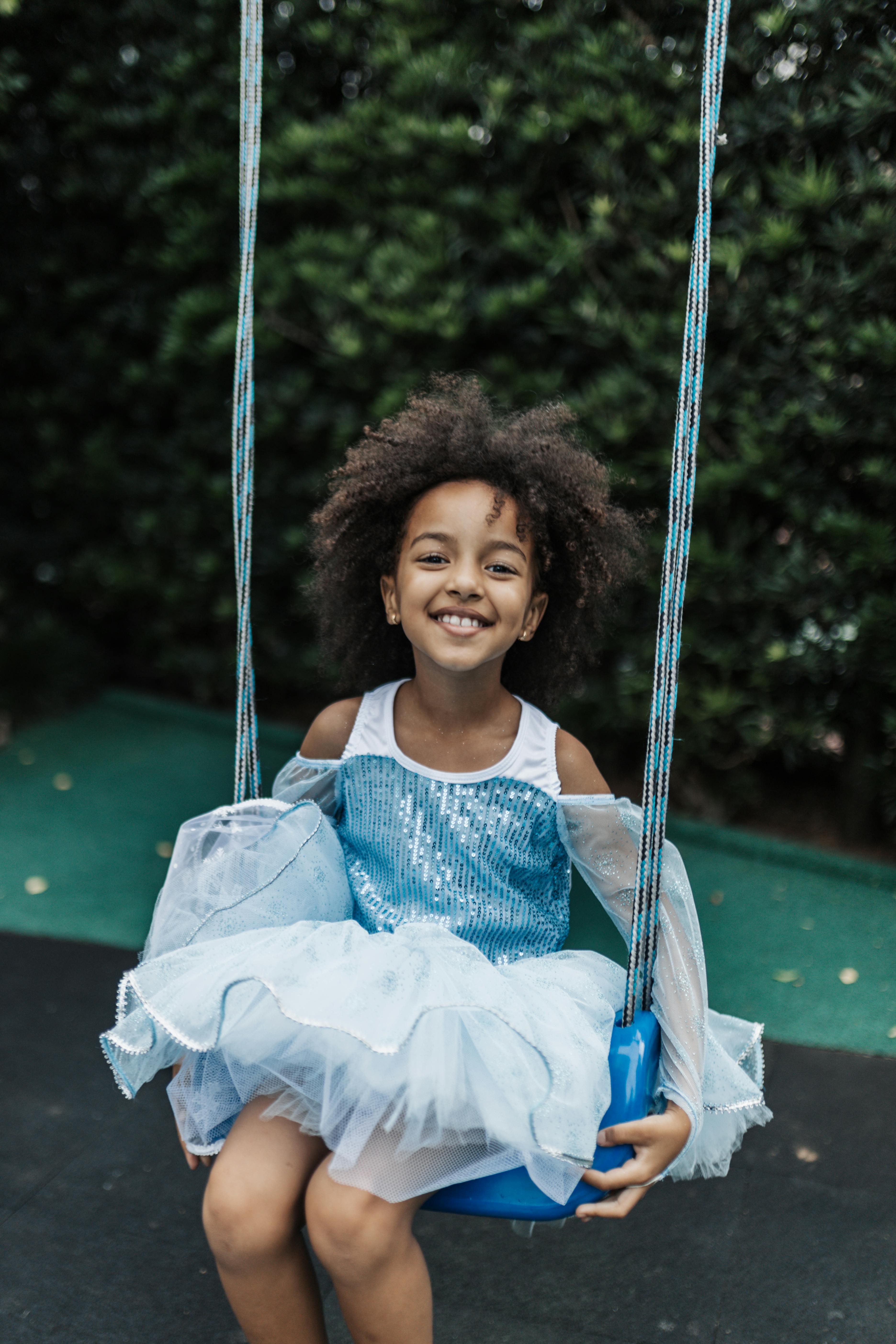 Smiling young girl in a blue dress enjoying a playful swing outdoors.