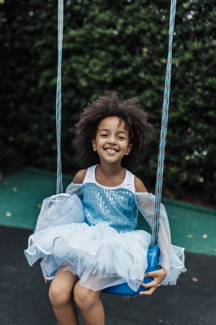Smiling young girl in a blue dress enjoying a playful swing outdoors.