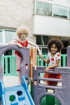 Diverse kids holding hands and smiling while playing on colorful playground equipment.