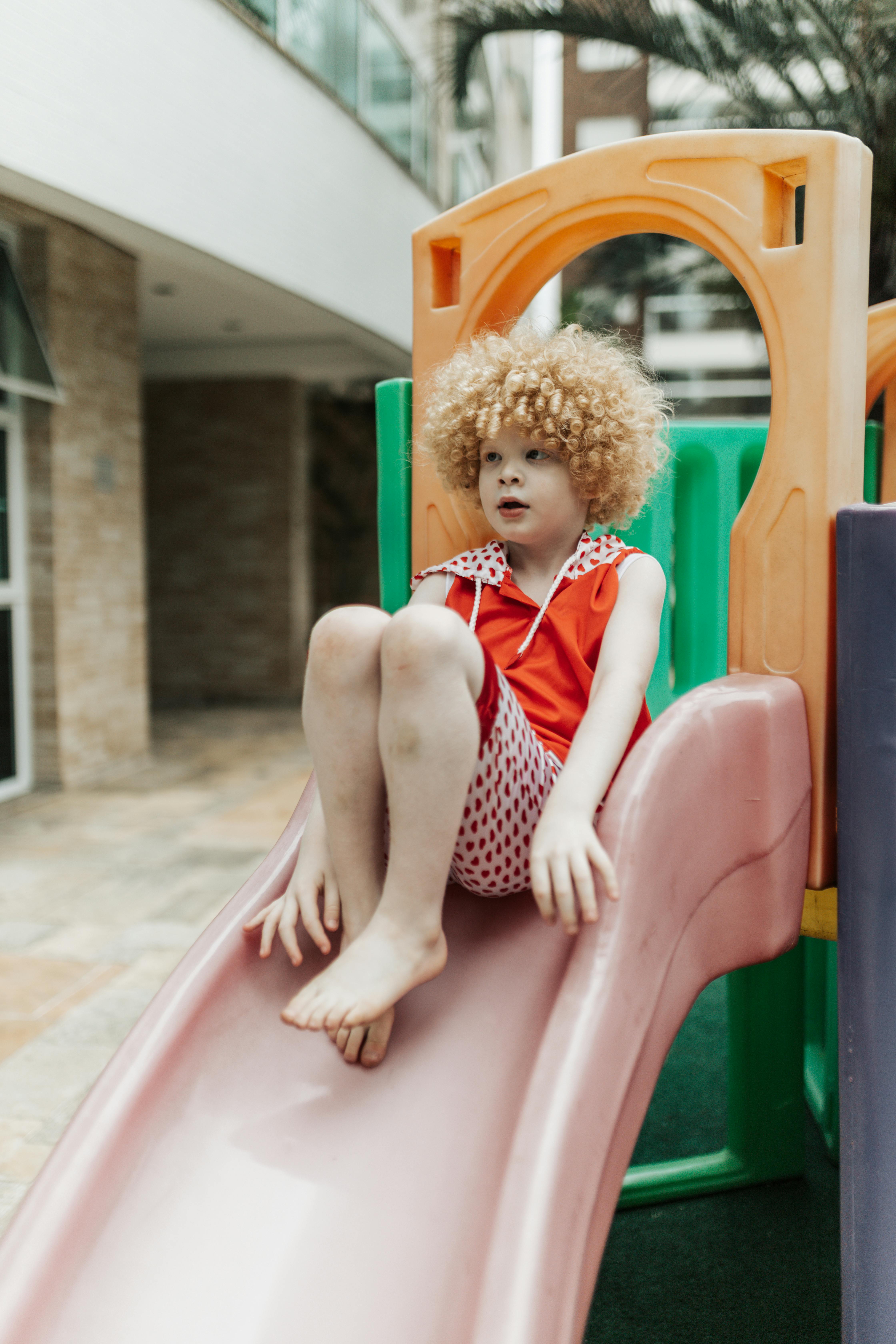 A Little Girl Sliding Down A Green Slide At The Playground. by