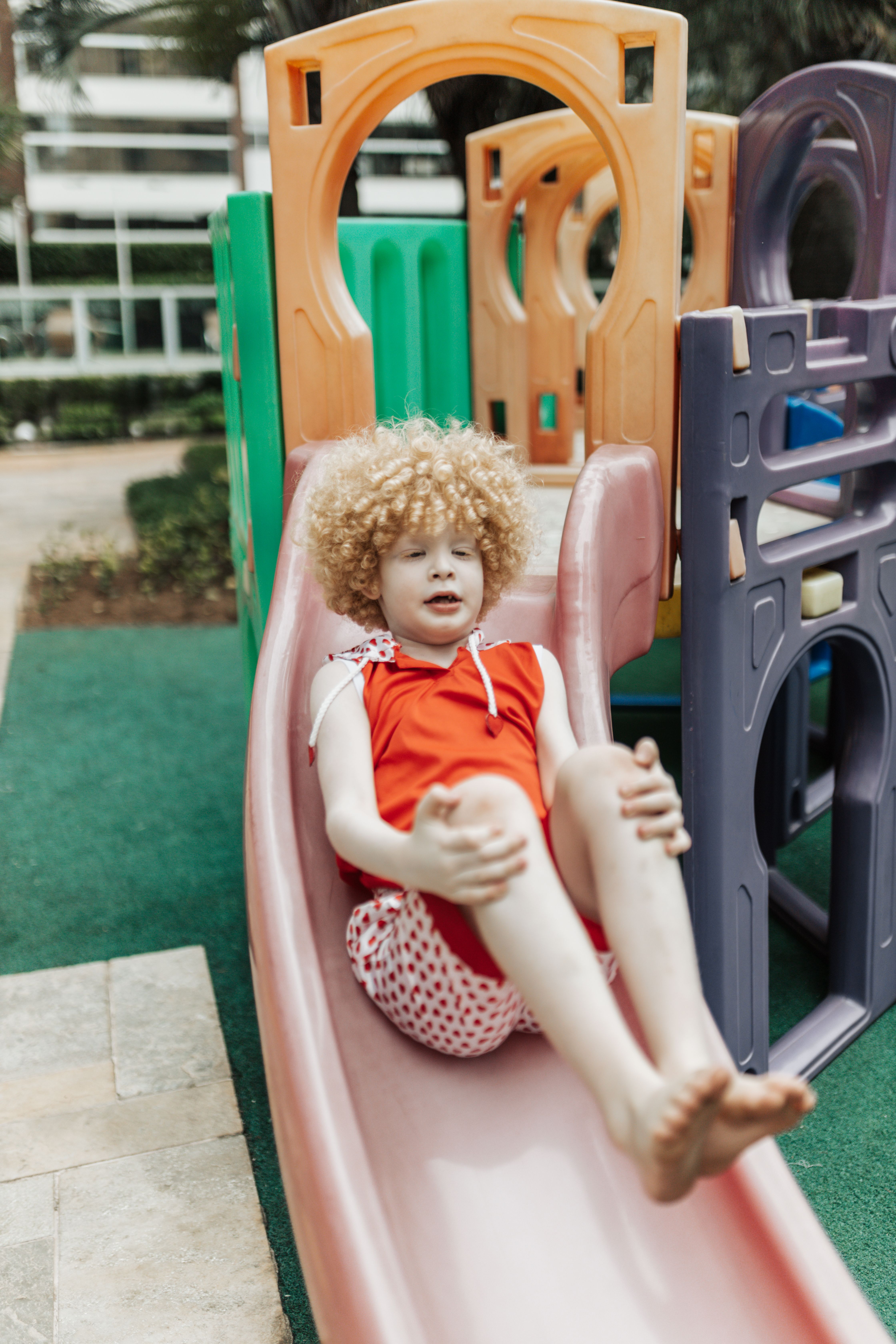 Smiling child with curly hair enjoying slide at outdoor playground.