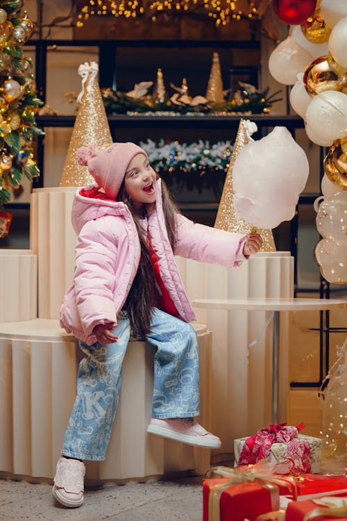 Girl in Pink Jacket, Beanie Hat, and Blue Pants Holding a Cotton Candy