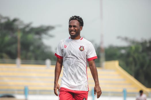 A joyful male soccer player on an outdoor field during the day, wearing a white jersey.