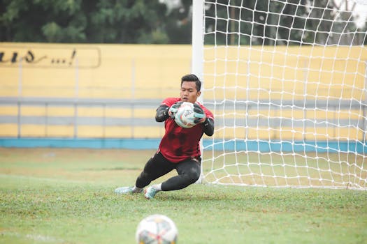 A soccer goalkeeper making a dynamic save during a game outdoors in Jakarta, Indonesia.