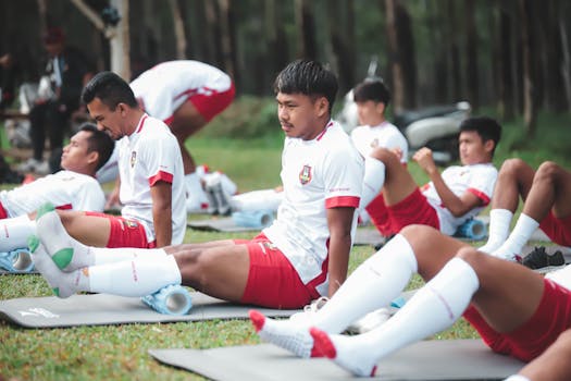 Football players in a training session doing stretches on a field in Jakarta.