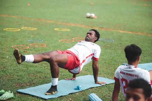 A man doing exercises on a mat in a field