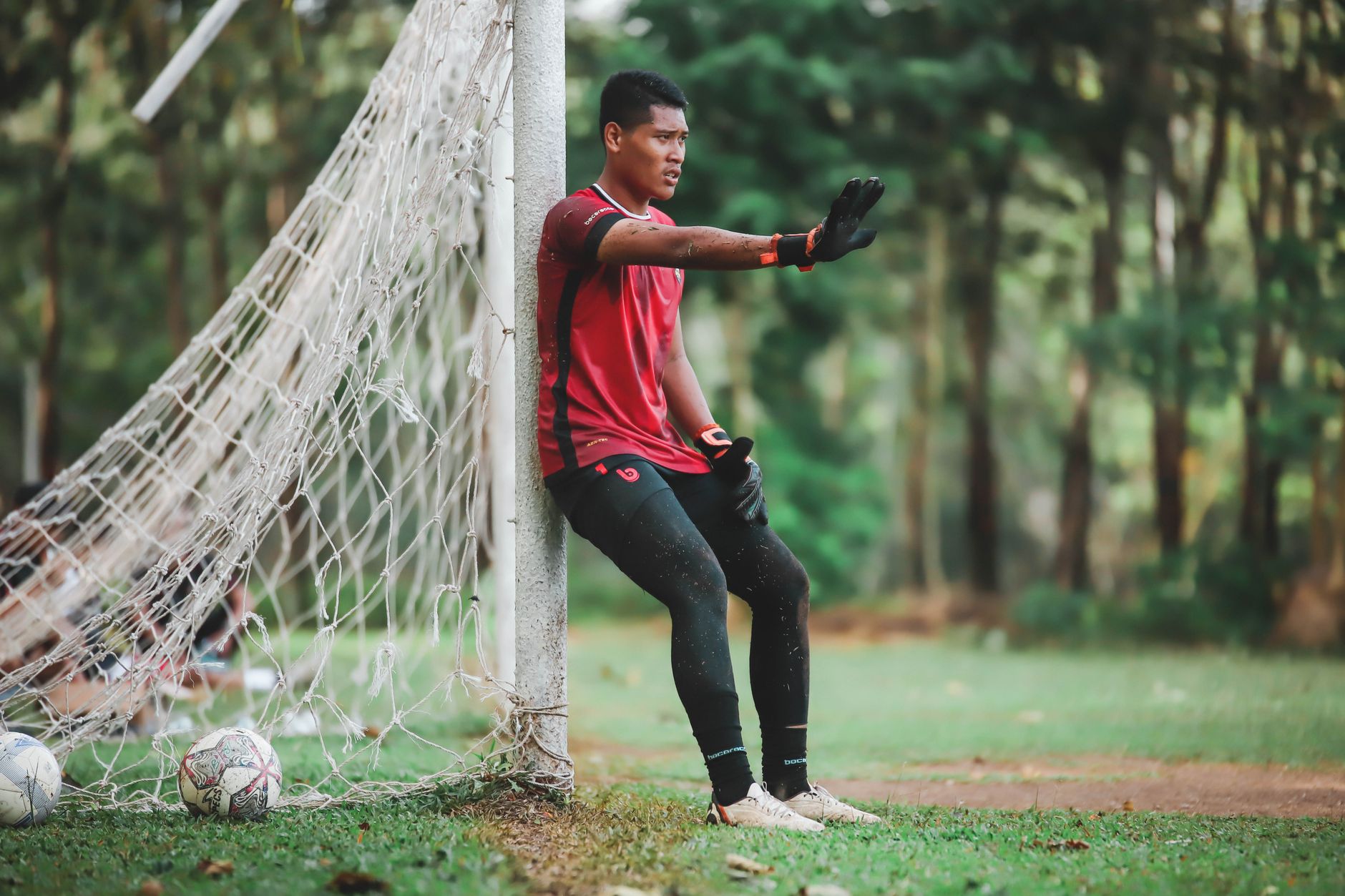 Indonesian football player eating rice and grilled chicken beside a training pitch at sunset