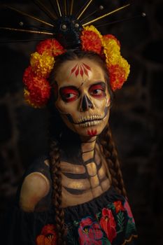 Artistic portrait of a woman with traditional Day of the Dead makeup and floral garland.