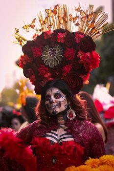 Woman in elaborate Day of the Dead costume with floral headpiece and skull makeup.