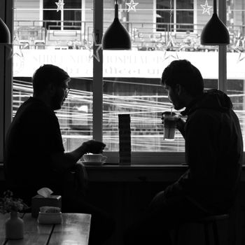 Black and white photo of two men seated near a window, enjoying coffee at a cafe.