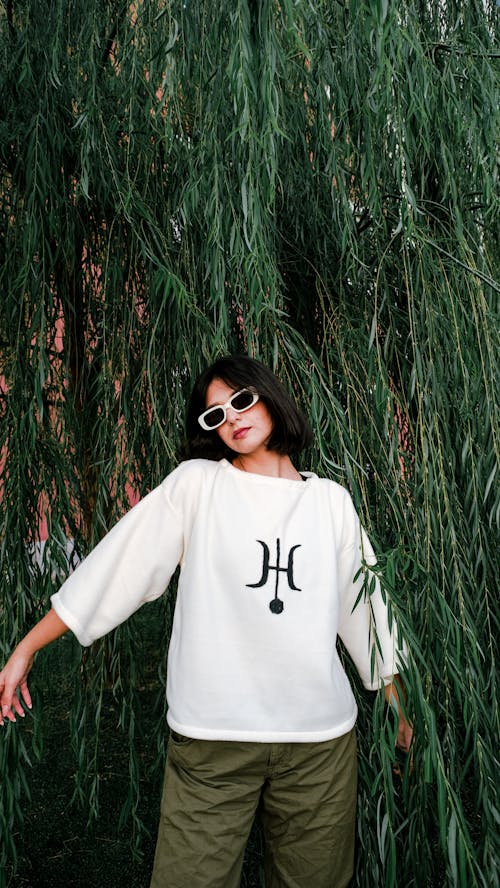 Model in White Fleece Printed Sweatshirt and Olive Pants in Front of a Willow Tree