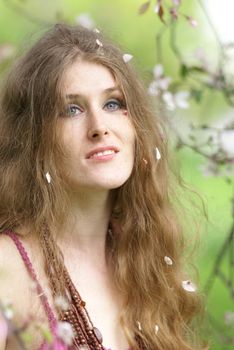 Portrait of a young woman with flowing hair surrounded by spring blossoms outdoors.
